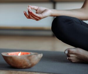 Close-up of a person's hand performing a yoga mudra next to a lit candle, evoking tranquility.