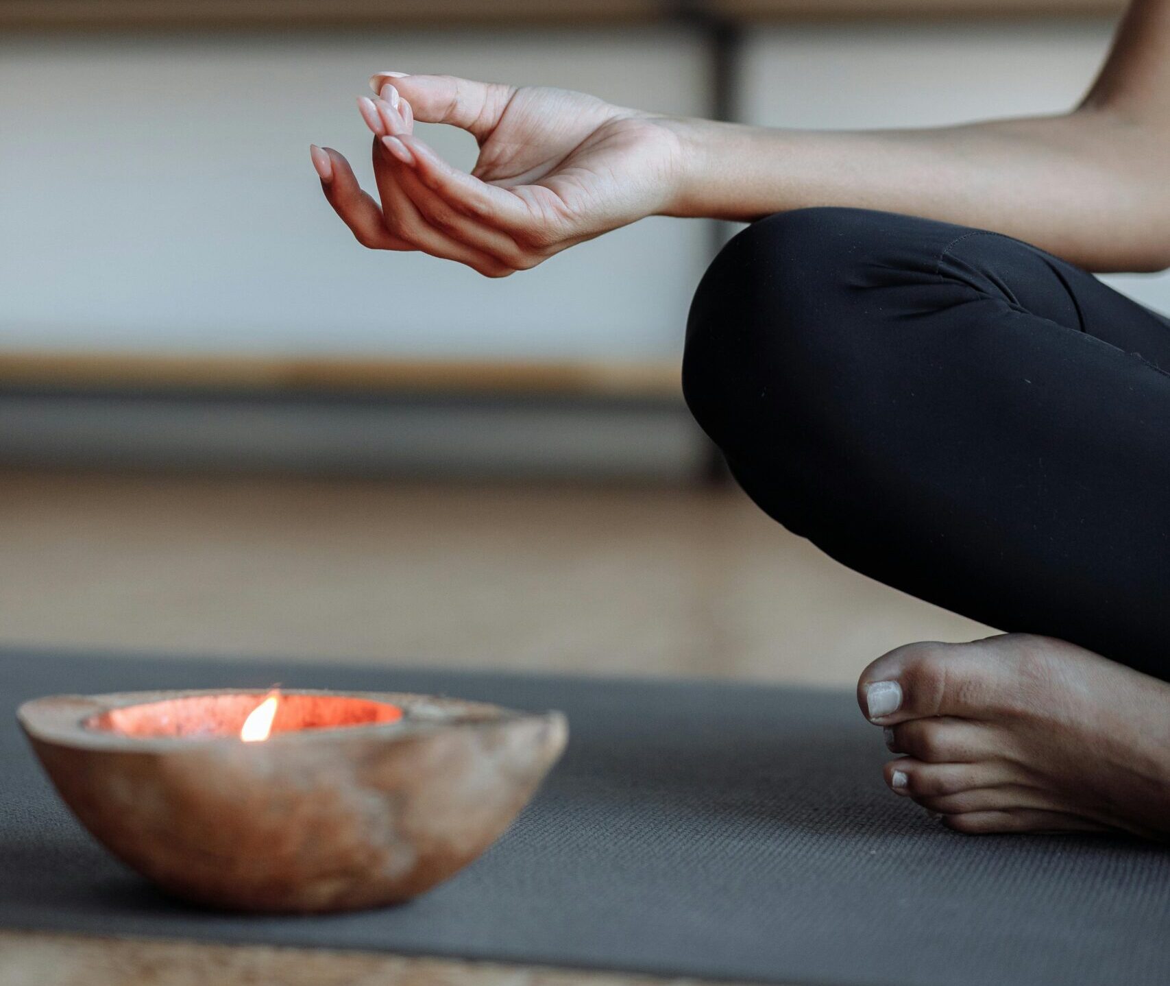 Close-up of a person's hand performing a yoga mudra next to a lit candle, evoking tranquility.